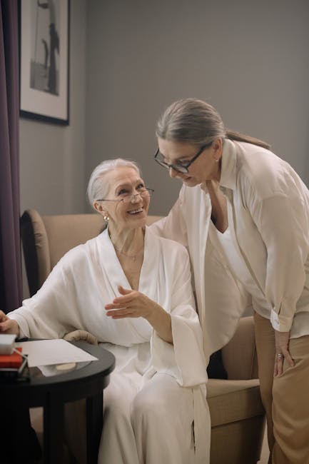 Two senior women in casual attire sharing a friendly conversation in a cozy room.